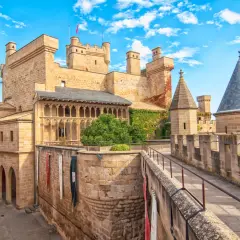 Imponente fortaleza de los castillos de España, con torres cónicas y un patio bajo un cielo azul y nubes blancas.