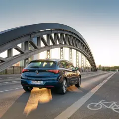 Ciemnoniebieska Astra jedzie po moście pod zachodzącym słońcem. Dostępne akcje serwisowe Opel dla Twojej Astry.