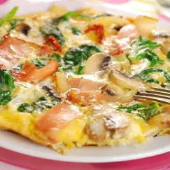 Omlet z szpinakiem, pieczarkami i bekonem na białym talerzu, widelcem.