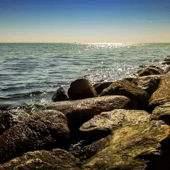 Kamienista plaża, fale rozbijające się o brzeg. W oddali widać statki i horyzont. Idealne miejsce na spacer w miejscowościach obok Ustki.