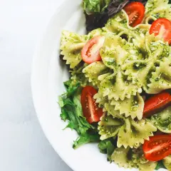 Un piatto invitante di pasta fredda al pesto, con farfalle condite e pomodorini freschi, guarnito con insalata verde.