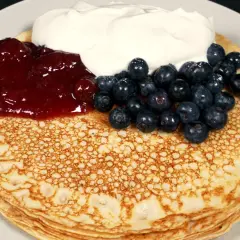 En hög med glutenfria pannkakor toppas med sylt, blåbär och grädde.