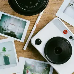 A white Leica Sofort 2 camera with instant photos scattered around. This setup inspires ideas on how to organize photos into folders.