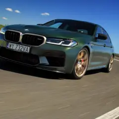 Zielony BMW M5 CS na zakręcie drogi pod błękitnym niebem.