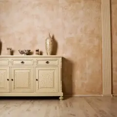 Inspiracje glinką wenecką: kremowa komoda z crackle, wazony i misy na tle ściany o rustykalnej fakturze.