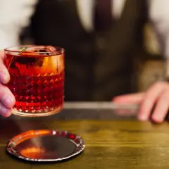 Ein Barkeeper reicht einen roten Cocktail mit Eis und Garnitur. Perfekt, um cocktail mixen lernen.