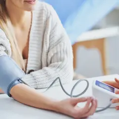 Kobieta z mankietem ciśnieniomierza na ramieniu, zastanawia się, czy ashwagandha obniża ciśnienie.