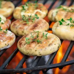 Des rondelles d'artichaut au barbecue, garnies de thym frais, grillent sur des braises ardentes.