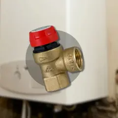 Gros plan sur un montage soupape de sécurité chaudière en laiton avec un capuchon rouge, installé sur une chaudière blanche.