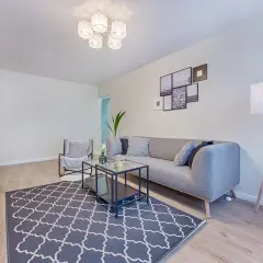Nowoczesne lampy sufitowe do niskich pomieszczeń rozświetlają salon z szarą kanapą i geometrycznym dywanem.