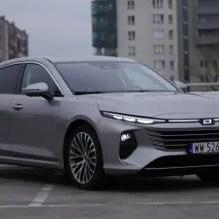 Srebrny Bestune B70 z nowoczesnymi światłami LED zaparkowany na betonowym placu, w tle budynki mieszkalne.