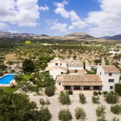 El cortijo el serbal, rodeado de olivos y montañas, con piscina azul y casas blancas de tejados terracota.