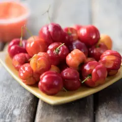 Talerz pełen soczystych, czerwonych i pomarańczowych owoców, przypominających egzotyczną wiśnię krzyżówkę.