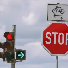 Ampel zeigt Rot, daneben ein Stoppschild. Wie lange halten? Radweg-Schild darüber.