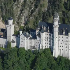 Bajkowy zamek w Niemczech, Neuschwanstein, wyrasta z zielonych lasów na tle skalistego zbocza.