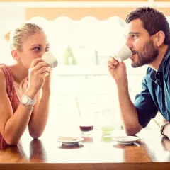 Coppia al bar, lui la guarda intensamente, un uomo innamorato in segreto che cerca il suo sguardo mentre bevono un caffè.