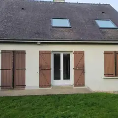Façade d'une maison année 80, caractéristiques : toit en ardoise, deux fenêtres de toit, porte-fenêtre blanche et volets en bois marron.