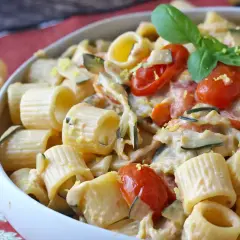 Piatto cremoso di pasta con zucchine, pomodorini e un tocco di Philadelphia, guarnito con basilico fresco.