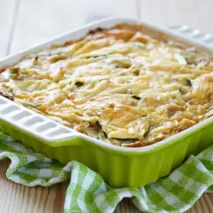 Pastel de calabacín horneado, con queso gratinado y rodajas de calabacín visibles, servido en un recipiente verde sobre un mantel a cuadros.