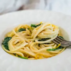 En gaffel lyfter en krämig portion pasta limone med gröna blad och citronskal.