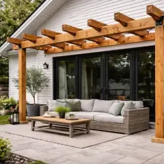 En nybyggd träpergola ger skugga och mysbelysning till en befintlig altan med soffgrupp och soffbord.
