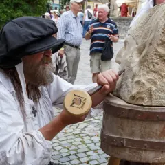 Steinmetz bei der Arbeit am Bad Wimpfen Zunftmarkt. Ein Mann mit Bart und schwarzer Kappe meißelt an einer Steinskulptur.