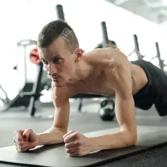 Un homme concentré effectue un gainage dynamique sur un tapis de gym, muscles tendus, dans une salle de sport.