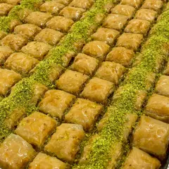En stor bricka med gyllene, krispiga baklavabitar, generöst strödda med gröna pistagenötter. Perfekt för ett hemlagat baklava recept.