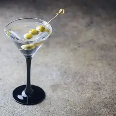Elegancki dirty martini z trzema oliwkami na wykałaczce, stojący na czarnej podstawie.