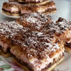 Pyszny pleśniak przepis babci. Warstwy ciasta, różowego kremu i czekolady, posypane kruszonką i cukrem pudrem.
