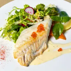 Filet de haddock parfaitement cuit, garni de perles de hareng, servi avec une salade fraîche, des légumes et une sauce crémeuse.