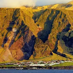 Un pueblo en Tristan de Acuña se asienta al pie de imponentes montañas cubiertas de hierba, bañadas por la luz dorada del atardecer.