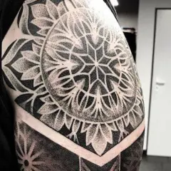 Imponujący tatuaż mandala na ramieniu, wykonany techniką dotwork. Wzór przypomina geometryczny kwiat, otoczony płatkami.
