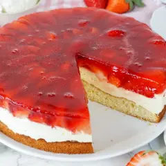 Erdbeerkuchen mit Biskuitboden, Vanillepudding und frischen Erdbeeren unter rotem Tortenguss. Ein Stück ist bereits angeschnitten.