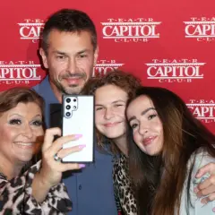 Katarzyna Skrzynecka z rodziną robi selfie. Uśmiechnięci rodzice i ich dzieci pozują na tle czerwonego banera z napisem "Teatr Capitol".