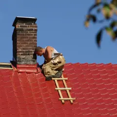 Handwerker auf einem roten Ziegeldach arbeitet am schornstein abdichten.