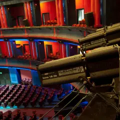 Wnętrze teatru z rzędami czerwonych siedzeń i balkonami. Reflektory oświetlają scenę. Ile miejsc ma teatr roma?
