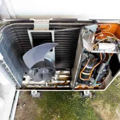 Unidad exterior de aire acondicionado abierta, mostrando el ventilador, el compresor y el cableado.