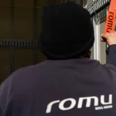 Persona con gorro negro asegura trincajes de cargas con una cinta naranja de la marca Romu.
