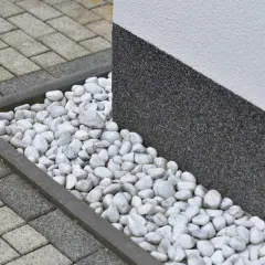 Grus runt huset med stenläggning och en mörk, strukturerad vägg.