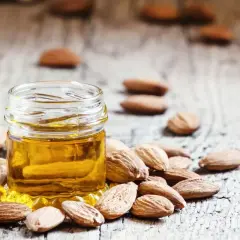 Un frasco de aceite de almendras para la cara rodeado de almendras enteras sobre una superficie de madera rústica.