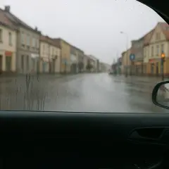 Widok z wnętrza samochodu na deszczową ulicę. Krople na szybie i wilgoć w samochodzie utrudniają widoczność.