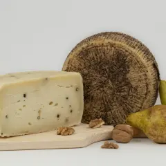 Varietà di tipi di pecorino, uno a spicchio con pepe nero, uno intero con crosta scura, pere e noci su tagliere di legno.