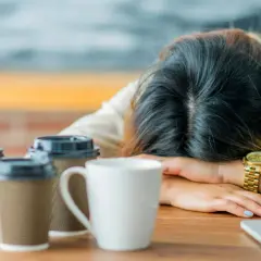 Erschöpfter Lehrer, Kopf auf dem Tisch, umgeben von Kaffeebechern. Die Anzeichen von **Lehrer Depression** sind deutlich.