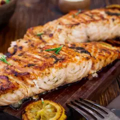 Två saftiga filéer av grillad fisk, perfekt kryddad med örter, serveras på en träbricka med citron och en gaffel.