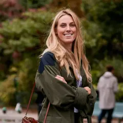 Mujer sonriente con un corte de pelo a capas, luciendo una chaqueta verde y un bolso de cuero.