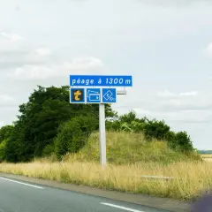 Panneau routier annonçant un péage à 1300m, avec symboles pour télépéage, cartes bancaires et espèces. La route Paris-Nantes se déroule sous un ciel nuageux.