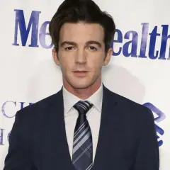 Drake Bell w garniturze, znany z filmów, seriali i programów, pozuje na tle wydarzenia charytatywnego.
