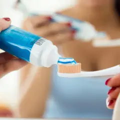 Ręka wyciska niebiesko-białą pastę na szczoteczkę. Szukając informacji, która pasta ma najwięcej fluoru, warto zwrócić uwagę na skład.