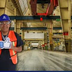 Hombre con casco y chaleco naranja sonríe en una nave industrial, sosteniendo un pulgar hacia arriba. Sus sistemas de limpieza son eficientes.